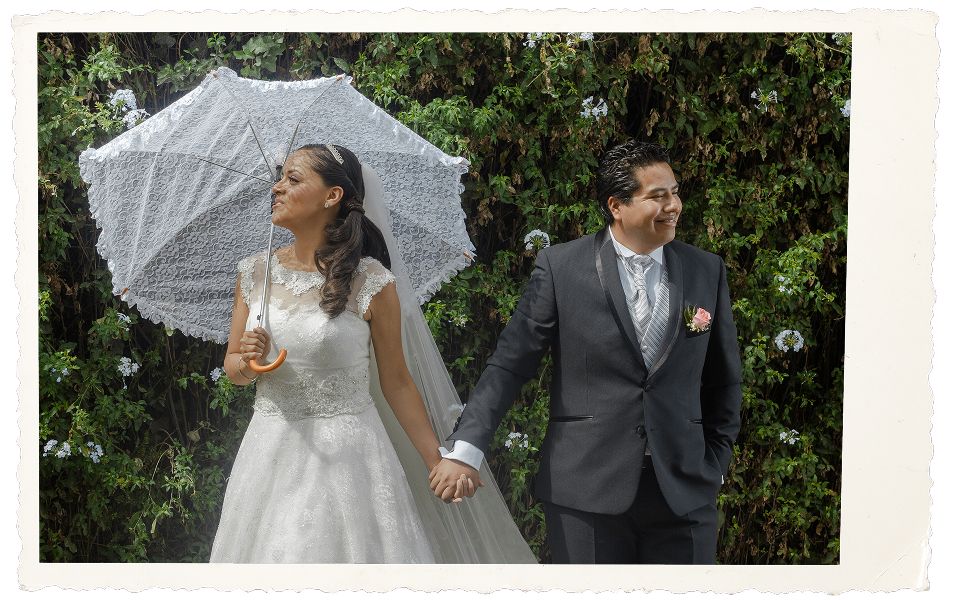 Novios caminando con sombrilla en jardín de bodas