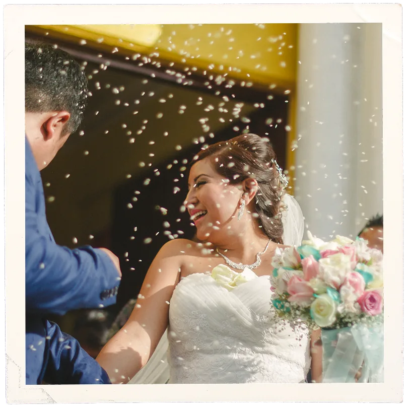 Novia riendo bajo una lluvia de pétalos con su ramo en la mano