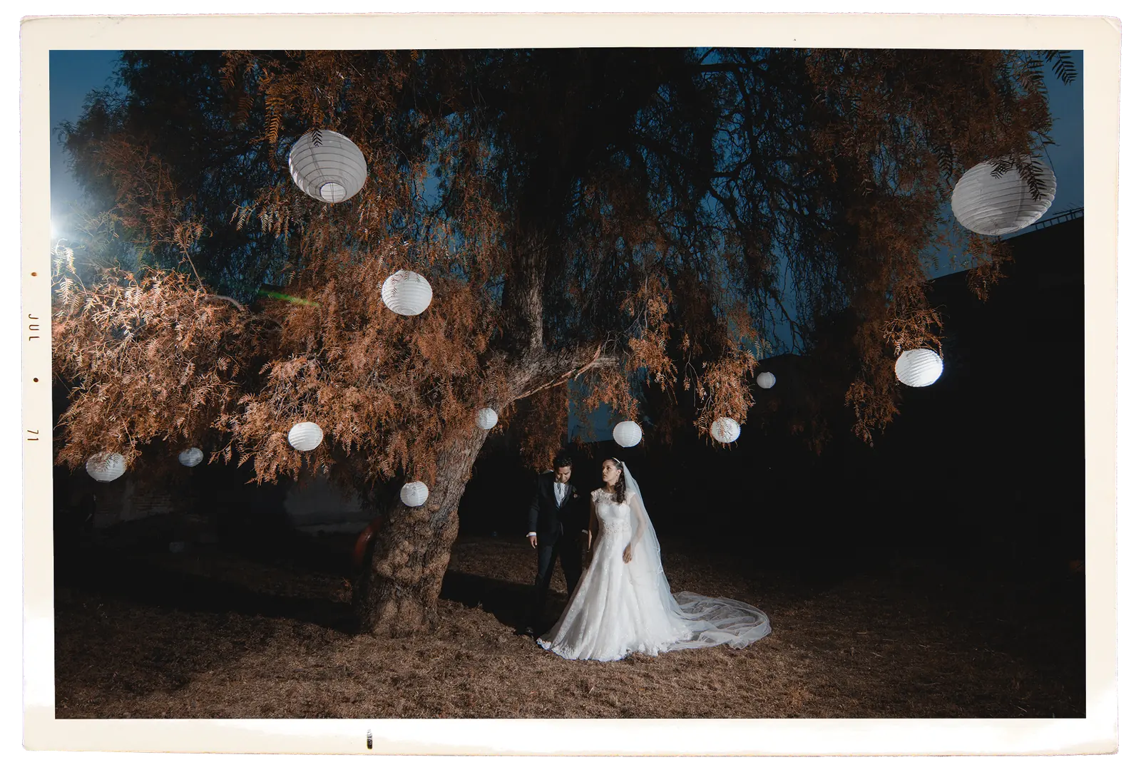 Los novios bajo un árbol con farolitos de papel por la noche