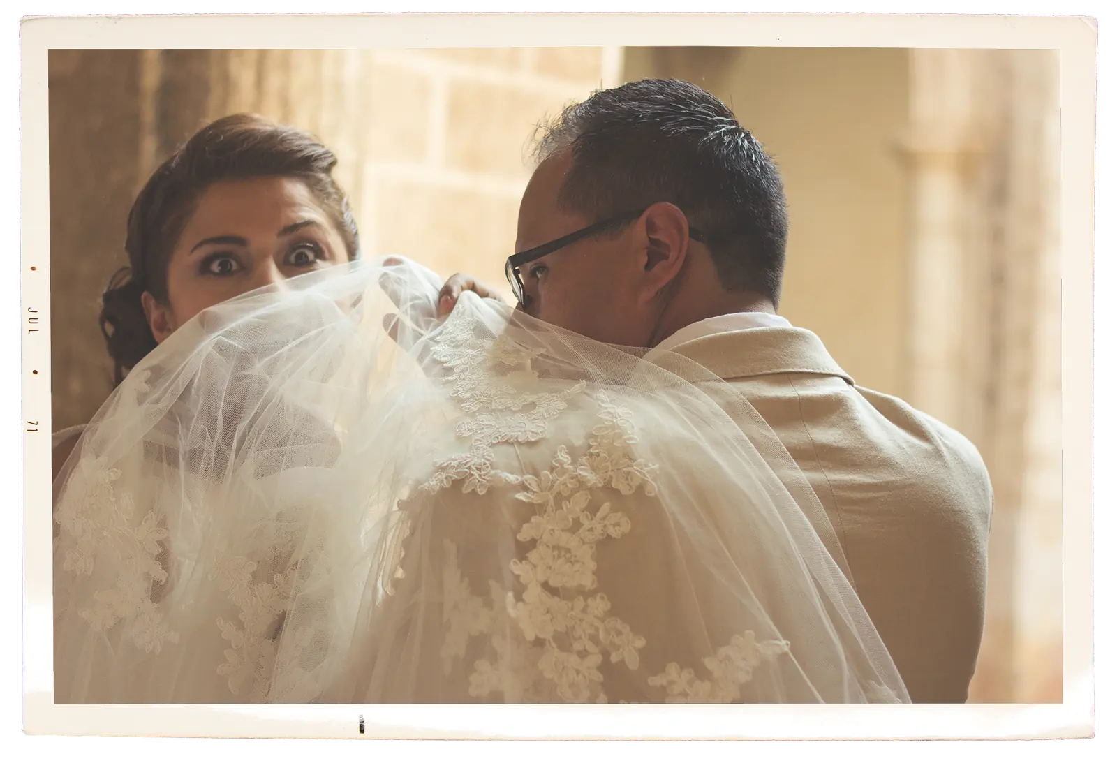 La novia se asoma sobre el hombro del novio, cubiertos por el velo